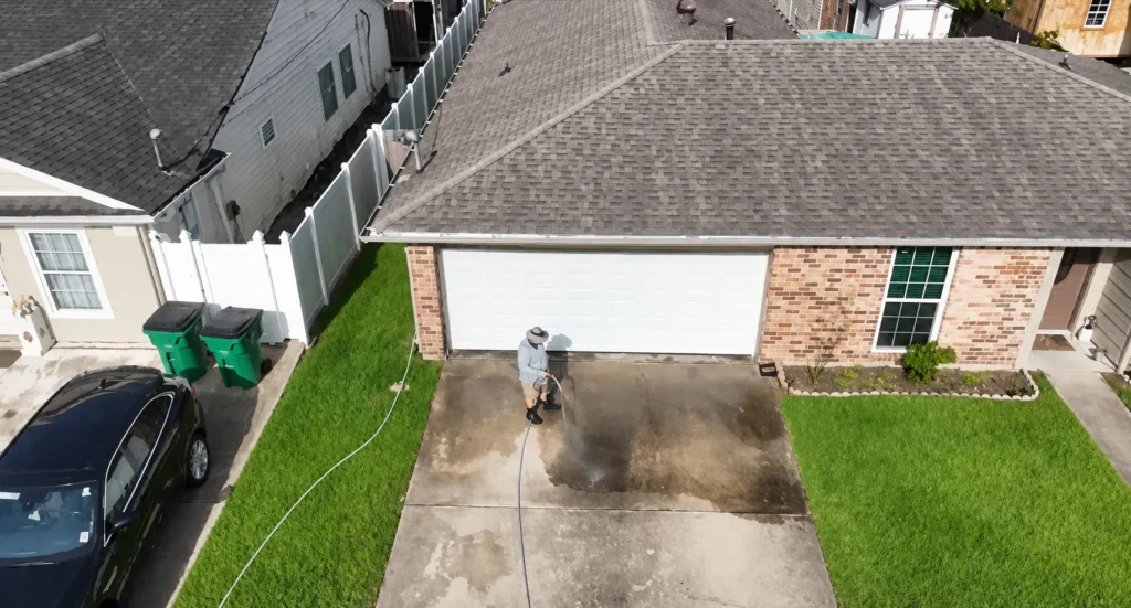 Worker using a pressure washer to clean a concrete driveway in front of a brick home - pressure wash in harvey