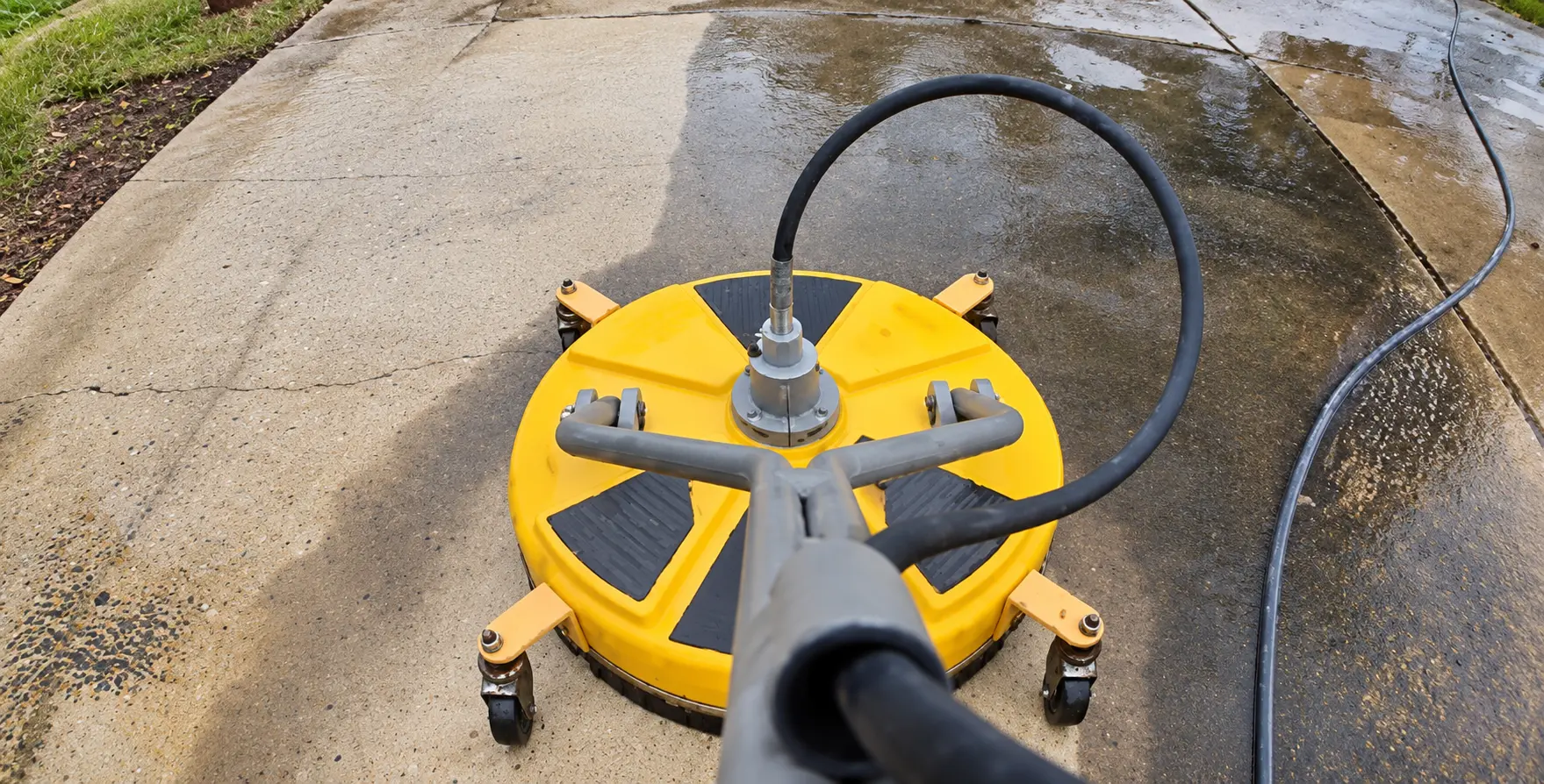 Yellow surface cleaner removing dirt and grime during a driveway pressure wash in Harvey